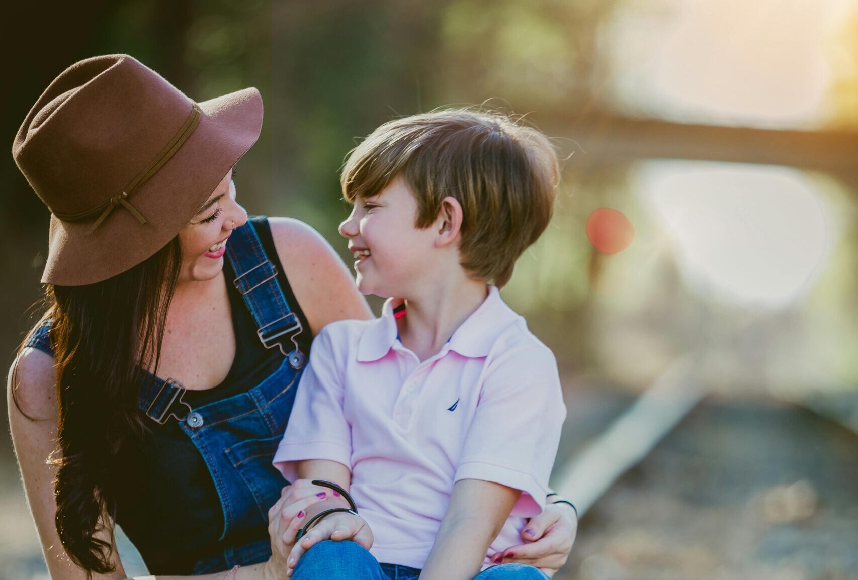 Mother and child sitting on railroad tracks, smiling at one another.